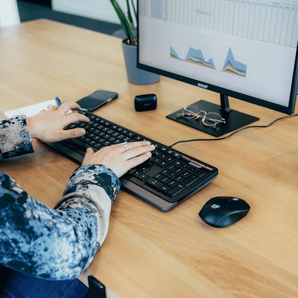 Personne utilisant un clavier Inovu noir azerty sur un bureau avec écran et souris.