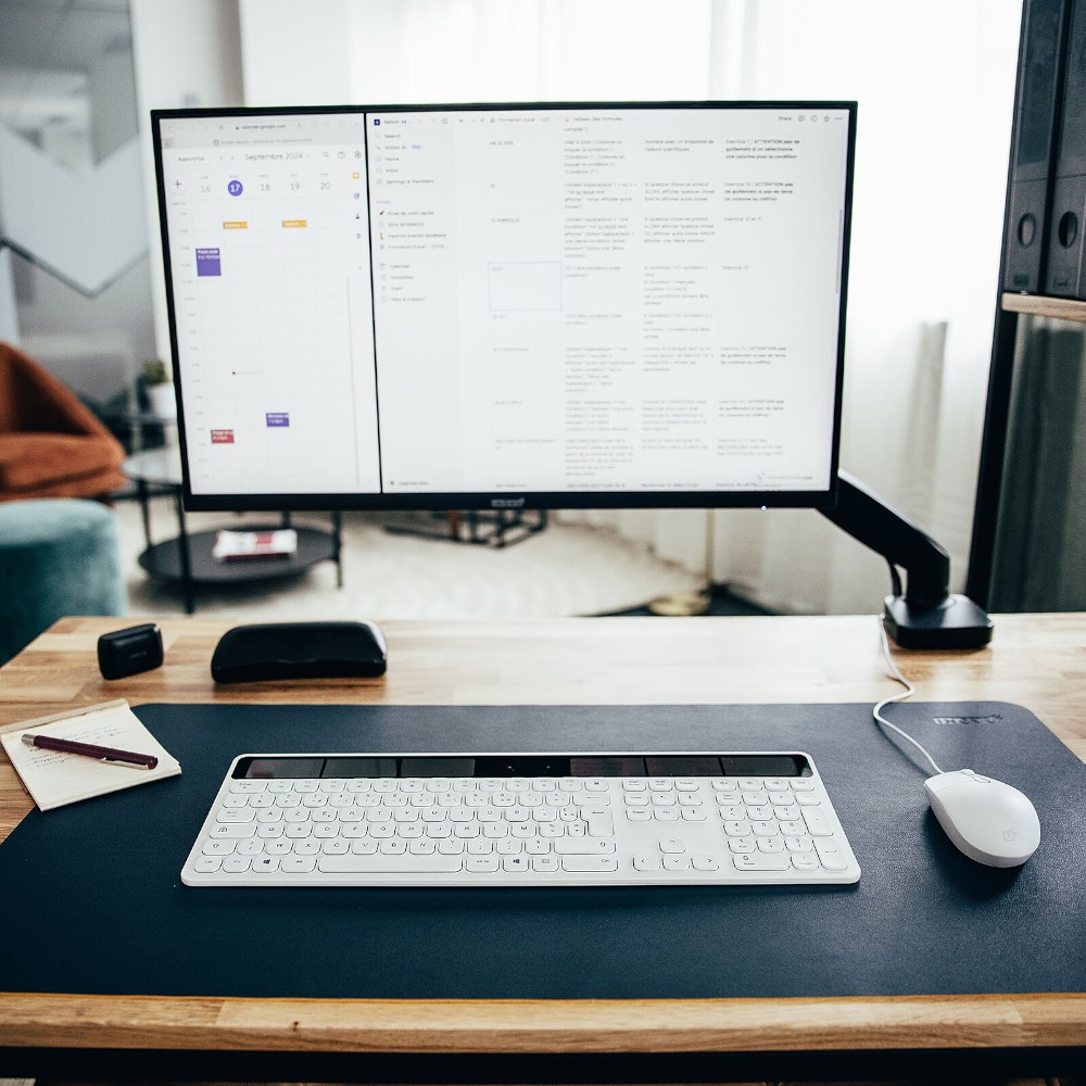 Tapis de souris bleu marine disposé avec un clavier et une souris sur un bureau en bois, avec un écran d'ordinateur.
