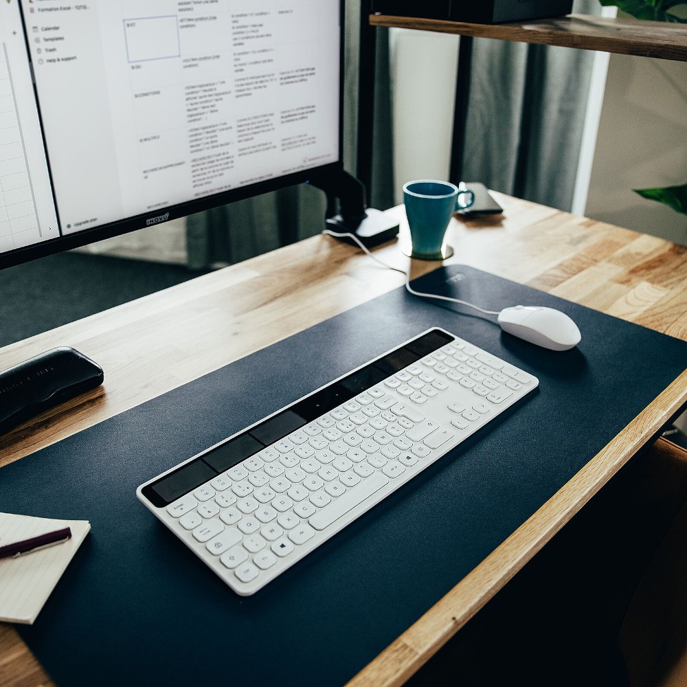 Tapis de souris bleu marine disposé sur un bureau en bois, avec un clavier blanc et une souris assortie.
