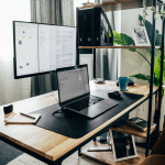 Tapis de souris noir disposé sur un bureau en bois, accompagné d'un ordinateur portable et d'un écran.
