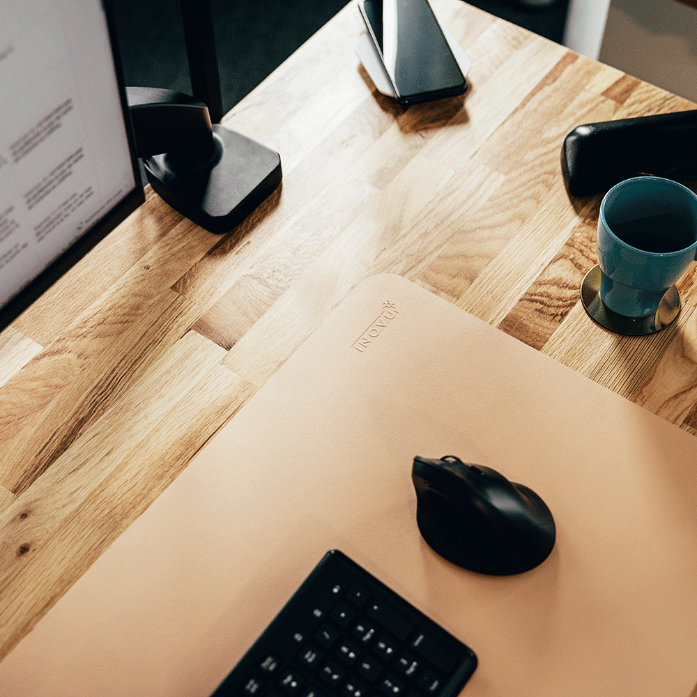 Tapis de souris beige disposé sur un bureau en bois, avec une souris noire et un clavier assorti.