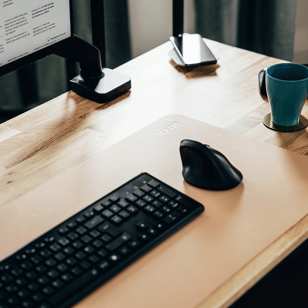 Souris verticale noire et clavier assorti posés sur un bureau en bois clair, avec une tasse à proximité.