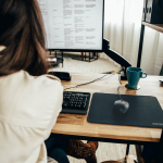 Personne utilisant une souris filaire noire sur un bureau en bois, avec un écran et un clavier.